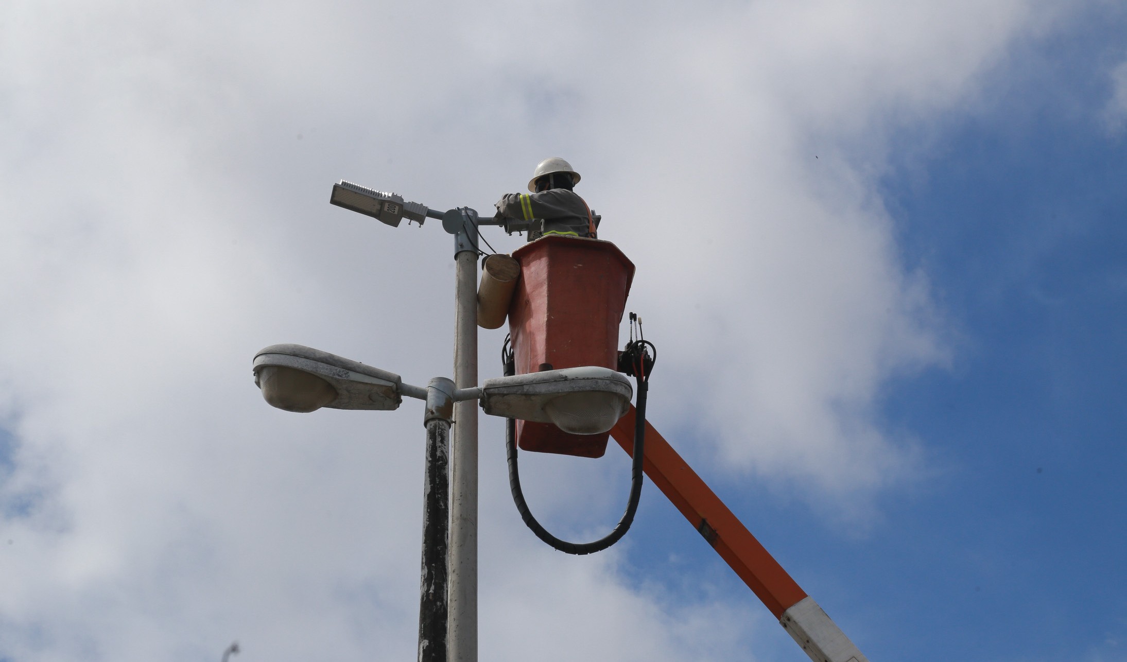 homem trocando uma lâmpada em um poste, ele está num guindaste de segurança